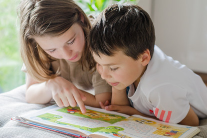 Das Bild zeigt 2 Kinder, die in einem Buch lesen.