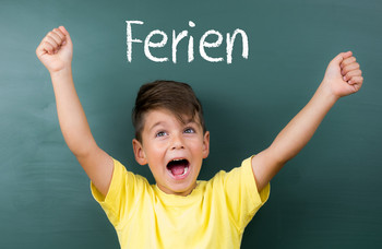 Ein Kind steht vor einer Tafel mit der Aufschrift Ferien.
