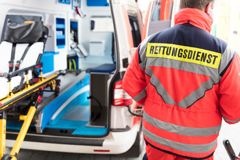 Das Bild zeigt einen Mann als Rettungsdienst neben einem Krankenwagen.