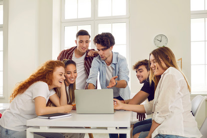 Junge Menschen sitzen und stehen um einen Laptop.